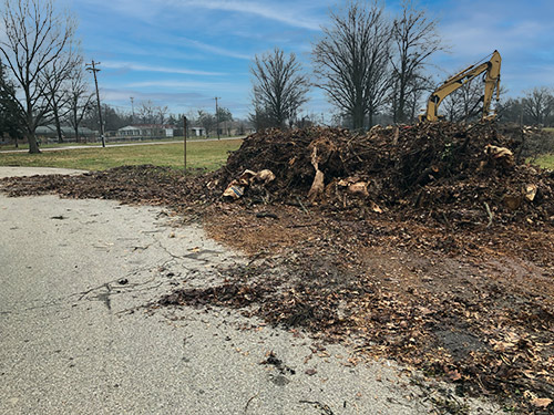 Landscape-Clean-Up Wood waste piled next to concrete lot with backhoe in background being used for landscape debris removal